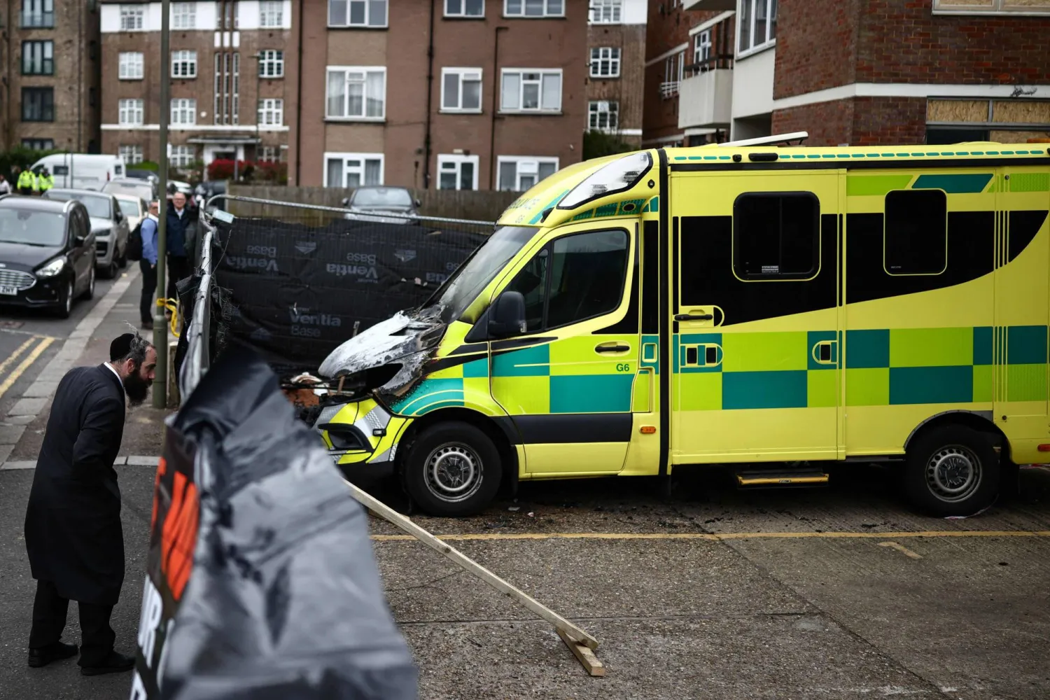 A member (L) of the Jewish community views the scene of an antisemitic arson attack through a makeshift fence in the Golders Green neighbourhood of north London, on March 24, 2026, a day after volunteer ambulances run by a Jewish organisation were set on fire. (Photo by Henry NICHOLLS / AFP)