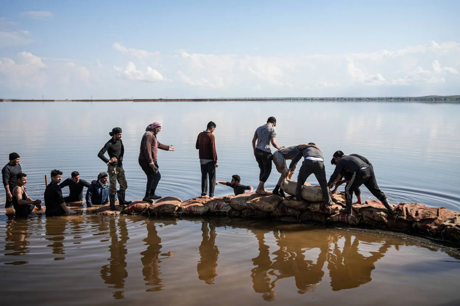 سكان الجزرايا جنوب حلب يملأون أكياس رمل لترميم سد ترابي منهار لمنع مياه الصرف الصحي المعالجة من إغراق المنازل والأراضي الزراعية المجاورة بعد هطول أمطار غزيرة (د.ب.أ)