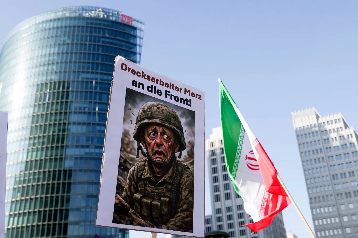 لافتة تحمل صورة المستشار الألماني فريدريش ميرتس خلال مسيرة تحت شعار «لا للحرب على إيران... السلام بدلاً من التضخم الناجم عن الحرب» بجانب العلم الإيراني في برلين (إ.ب.أ)