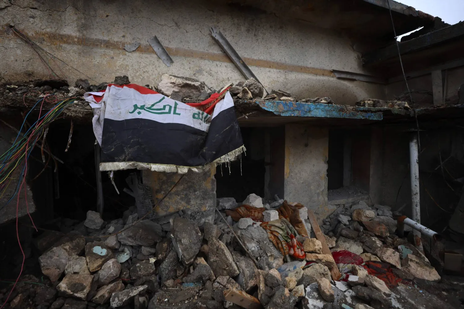 علم العراق معلقًا فوق الأنقاض في موقع مُدمَّر داخل قاعدة الحبانية العسكرية غرب البلاد (أ.ف.ب)