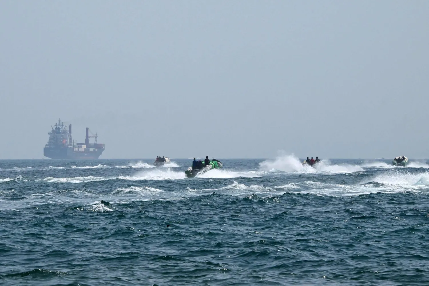 Small boats sail loaded with goods in front of a container ship in the waters of the Strait of Hormuz off the coast of Oman, June 25, 2025 (AFP)