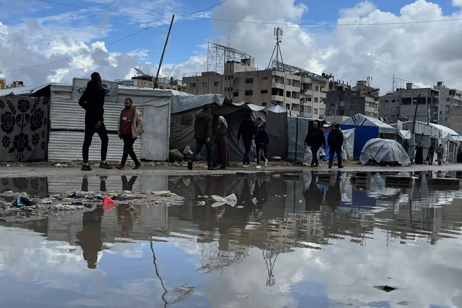 نازحون فلسطينيون يمشون إلى جانب خيامهم التي غمرتها مياه الأمطار في مدينة غزة يوم الخميس (د.ب.أ)