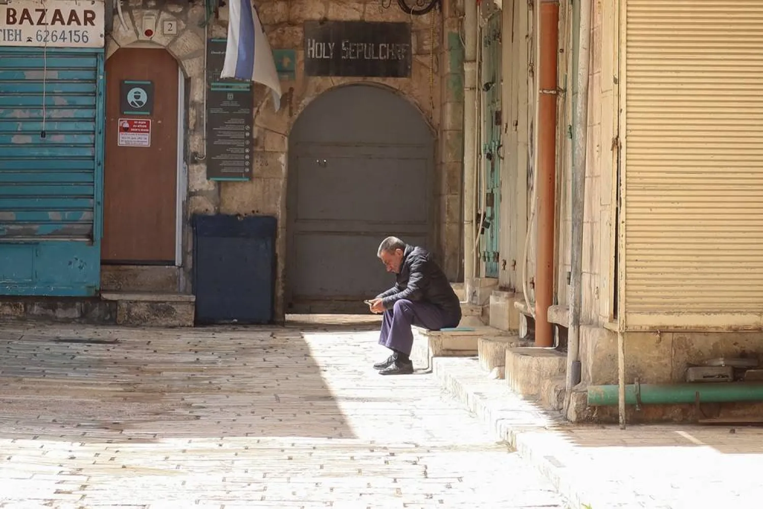  A man sits near a street in Jerusalem's Old City, following restrictions on large gatherings amid the US-Israel conflict with Iran, March 27, 2026. (Reuters)