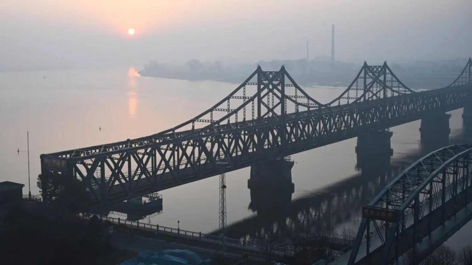 The sun rises over the North Korean town of Sinuiju, behind the Sino-Korean Friendship Bridge (L) and the Yalu River Broken Bridge (R), as seen from the border city of Dandong, in China's northeast Liaoning province on March 26, 2026. GREG BAKER / AFP
