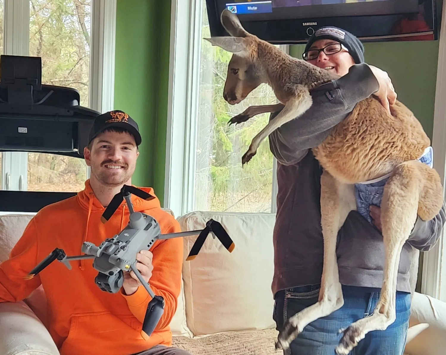 This photo provided by Cara Johnson shows her husband and drone operator, Colton Johnson, left, sitting next to Stacy Brereton as she holds a kangaroo named Chesney at Sunshine Farm, in Necedah, Wis., Saturday, March 28, 2026. (Cara Johnson via AP)
