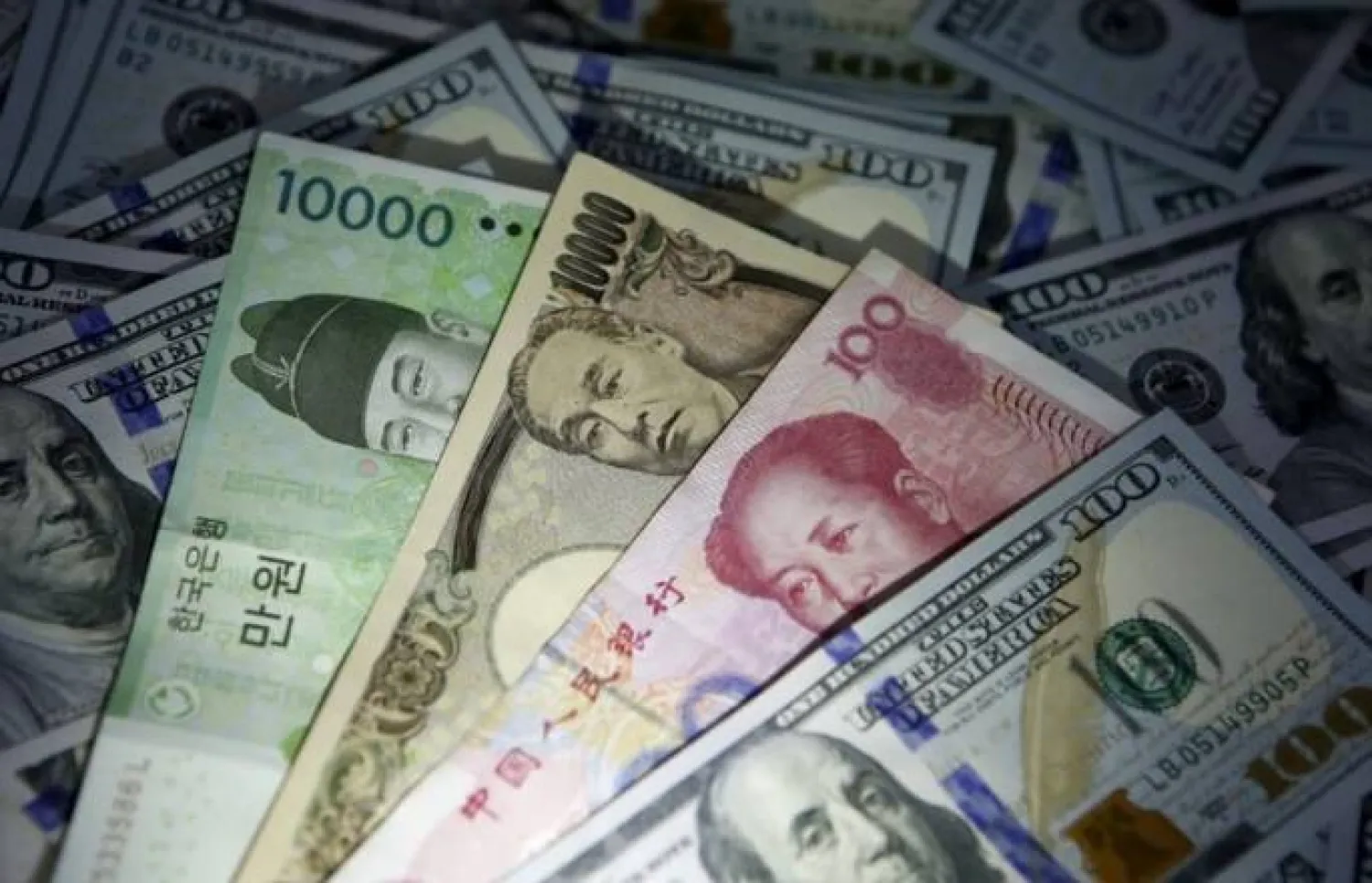 أوراق نقدية من الوون الكوري الجنوبي واليوان الصيني والين الياباني فوق أوراق نقدية من فئة 100 دولار أميركي (رويترز)