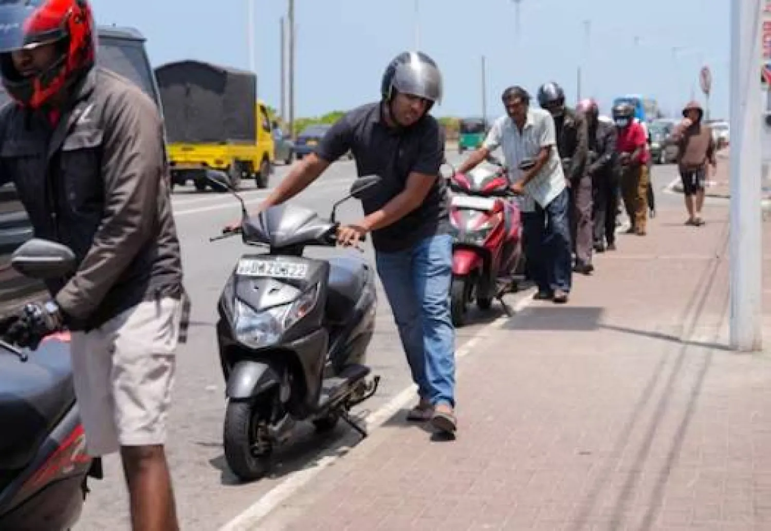 أشخاص يقفون في طابور أثناء انتظارهم لتزويد دراجاتهم النارية بالوقود في كولومبو (رويترز)