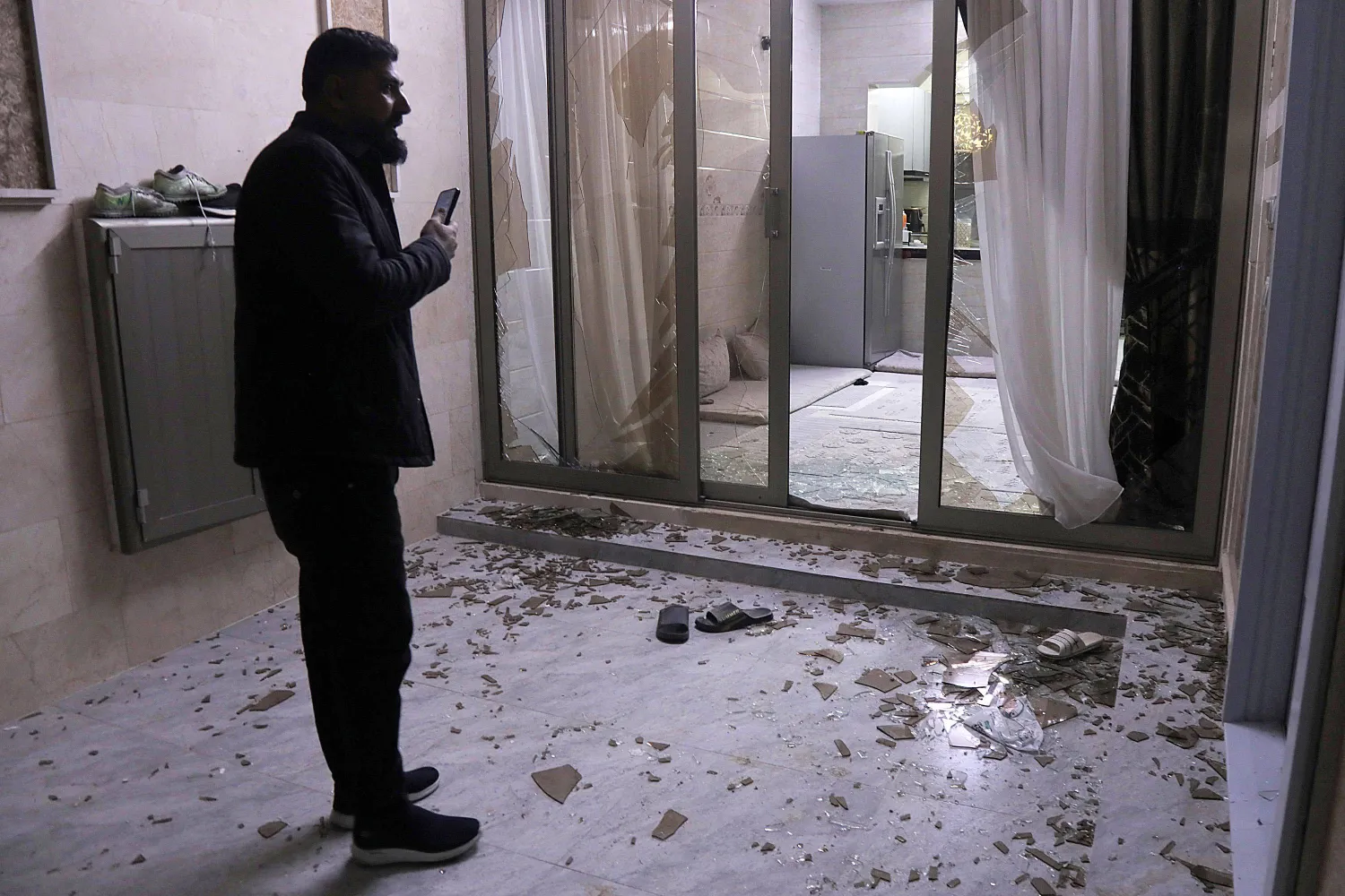 People inspect damage at a building whose windows were shattered following air defenses' interception of a projectile or drone over a residential neighborhood in Erbil, the capital of Iraq's northern autonomous Kurdish region, on March 4, 2026. (Photo by Safin HAMID / AFP)