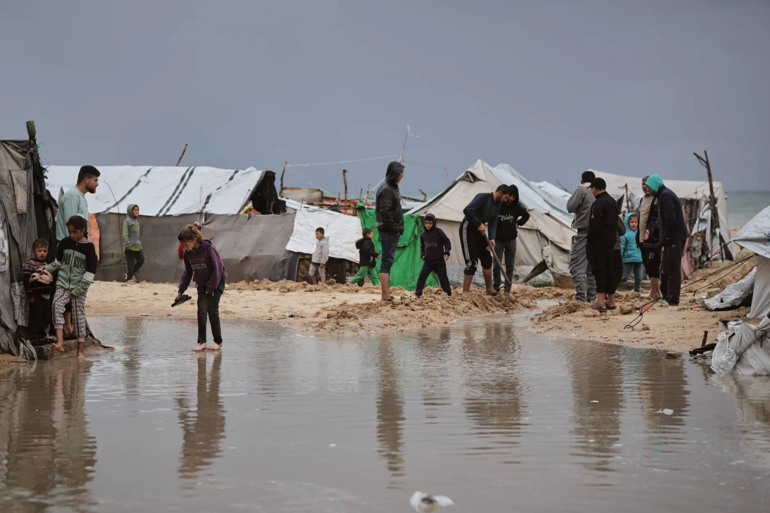 Palestinians walk through a flooded area in a temporary tent camp after heavy rainfall in Gaza City, Thursday, March 26, 2026 (AP Photo/Jehad Alshrafi)