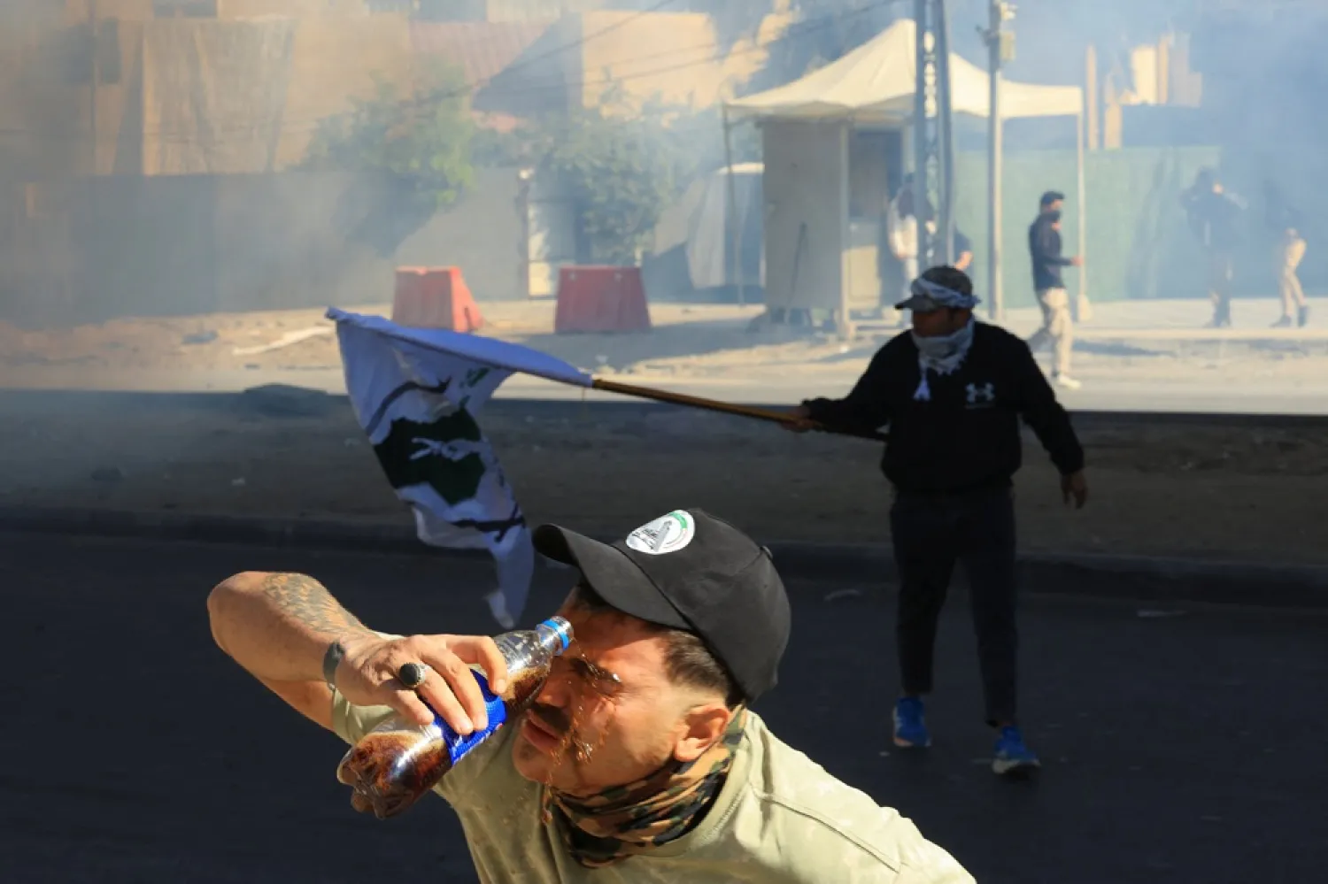 A person washes his face with a soft drink bottle after riot police deployed irritants to disperse protesters supporting Iraqi Shiite armed groups gathered near the entrance of the Green Zone and attempted to move toward the US embassy after the killing of Iran's Supreme Leader Ali Khamenei, in Baghdad, Iraq, March 1, 2026. (Reuters) 