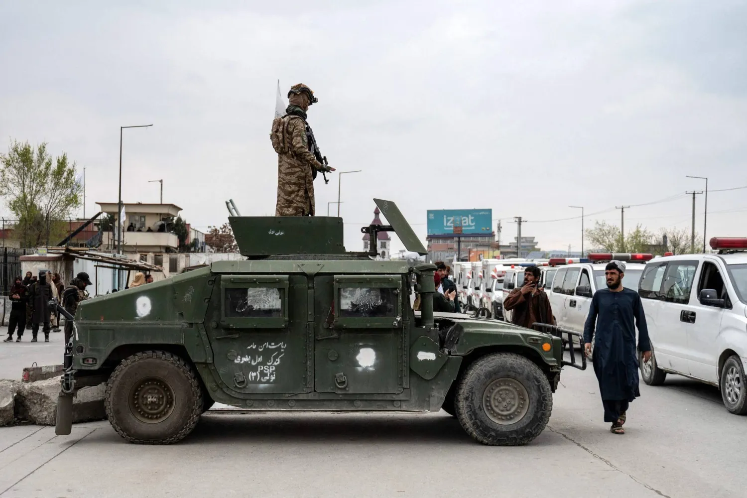 عنصر من «طالبان» يقف فوق مركبة مدرعة بينما تنقل سيارات الإسعاف توابيت ضحايا غارة جوية باكستانية في كابل (أ.ف.ب)