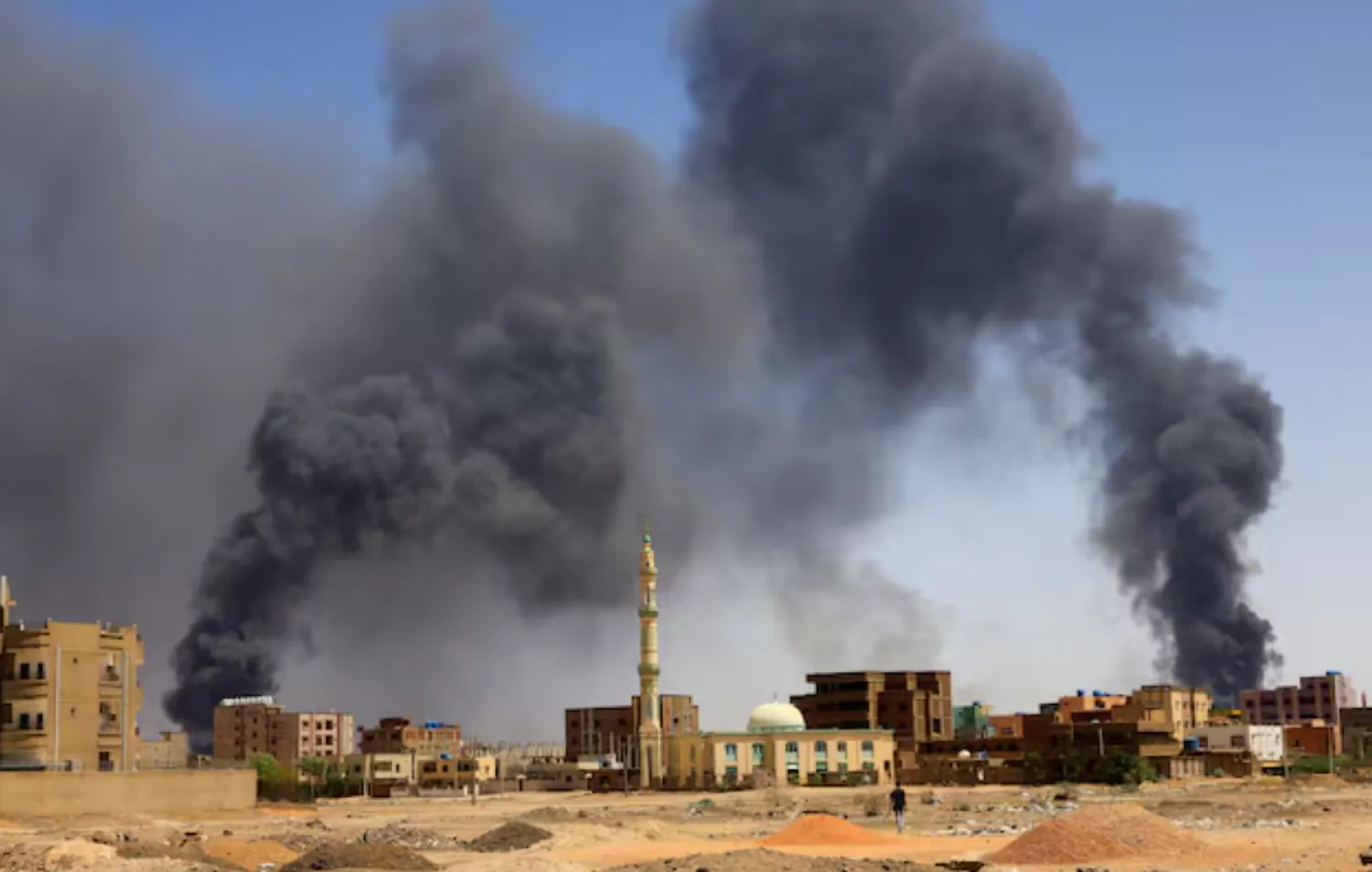 A man walks while smoke rises above buildings after aerial bombardment, during clashes between the paramilitary Rapid Support Forces and the army in Khartoum North, Sudan, May 1, 2023. REUTERS/Mohamed Nureldin Abdallah/File Photo