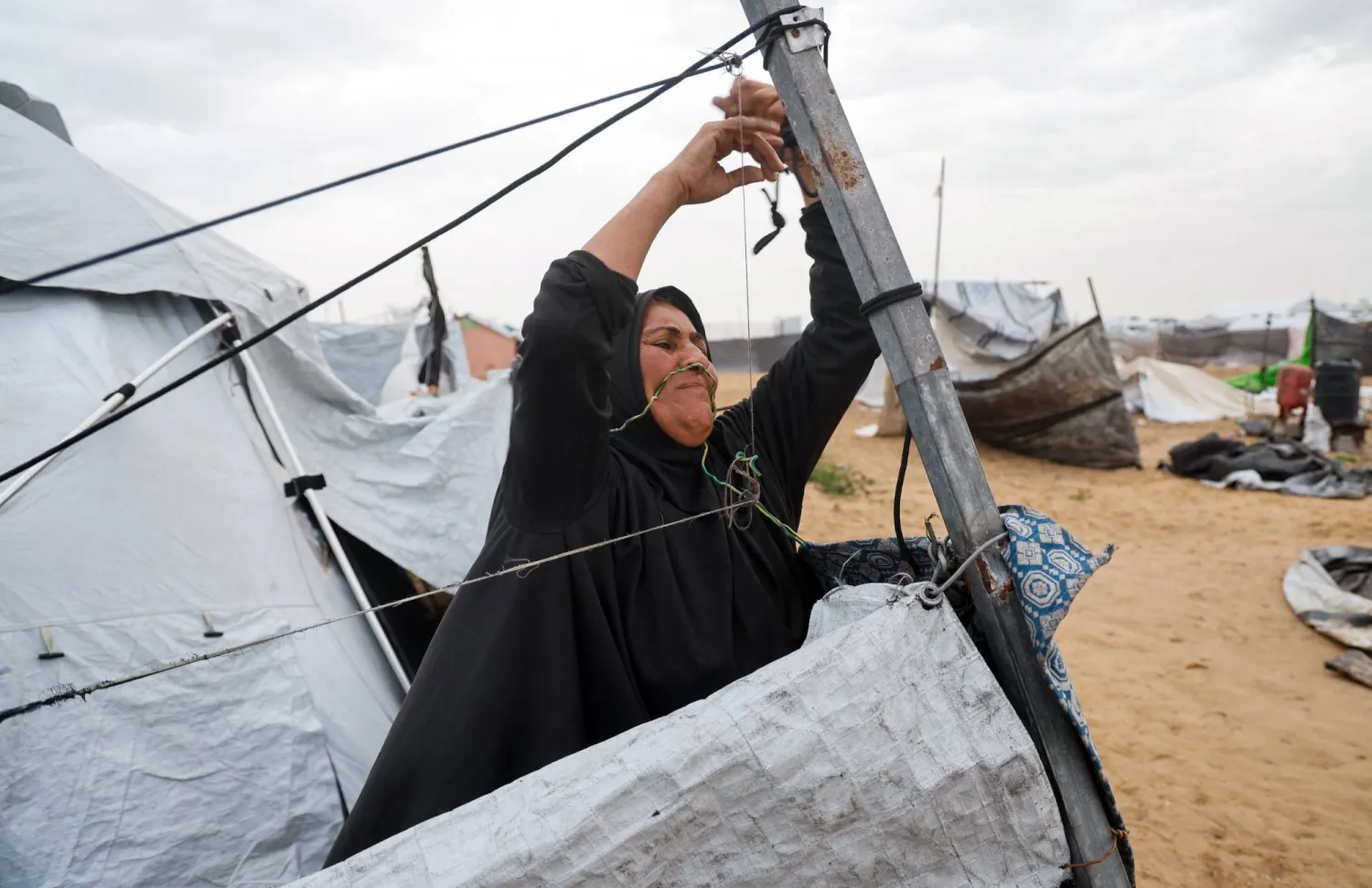 امرأة فلسطينية تشد دعائم خيمتها وسط يوم عاصف في خان يونس جنوب غزة الخميس (رويترز)