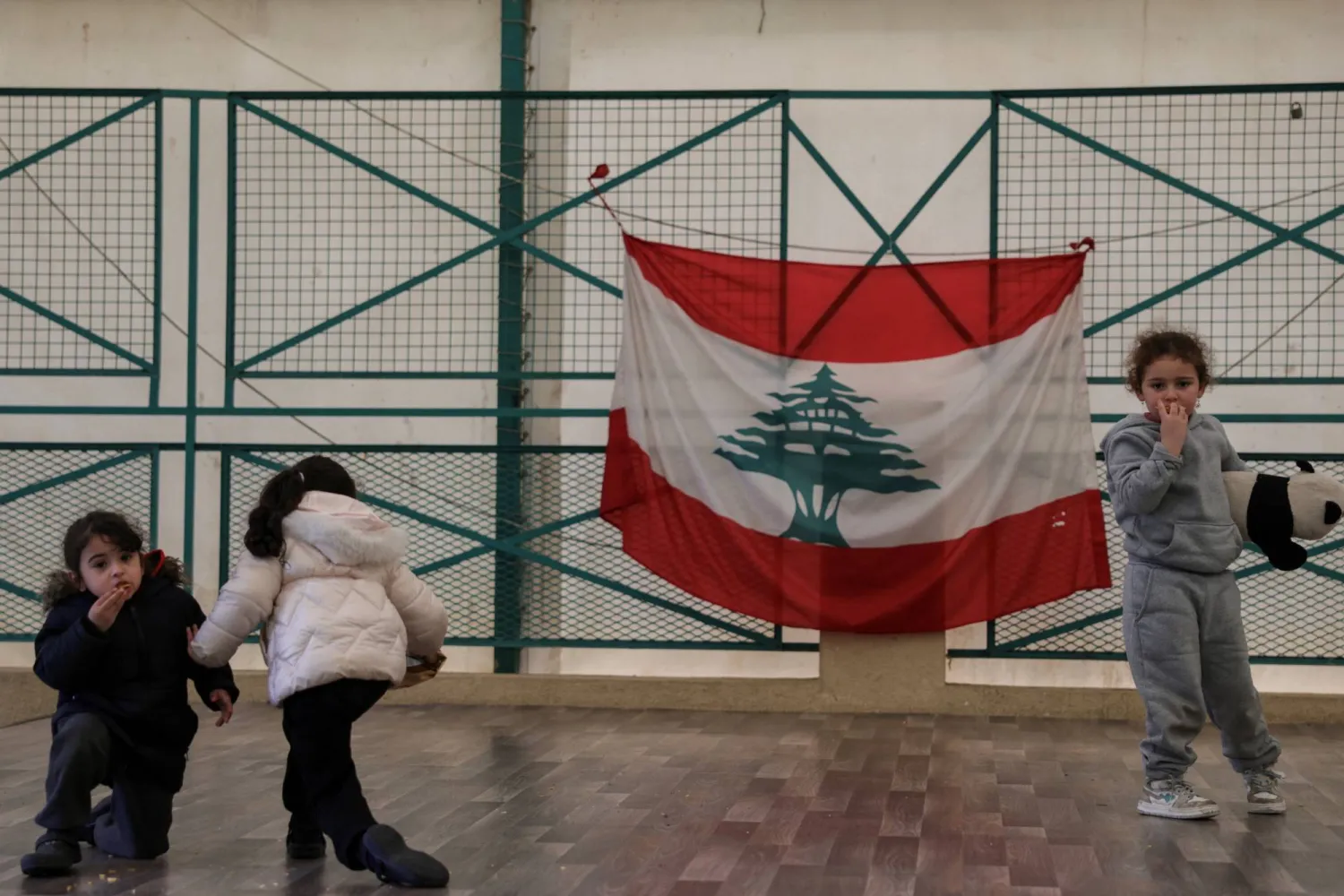 أطفال نازحون يلعبون في مدرسة تحولت إلى مركز للنزوح ومن خلفهم العلم اللبناني (رويترز)