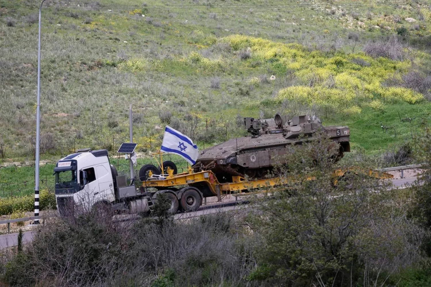An Israeli military truck transports a tank in the Upper Galilee in northern Israel near the Lebanese border (AFP) 