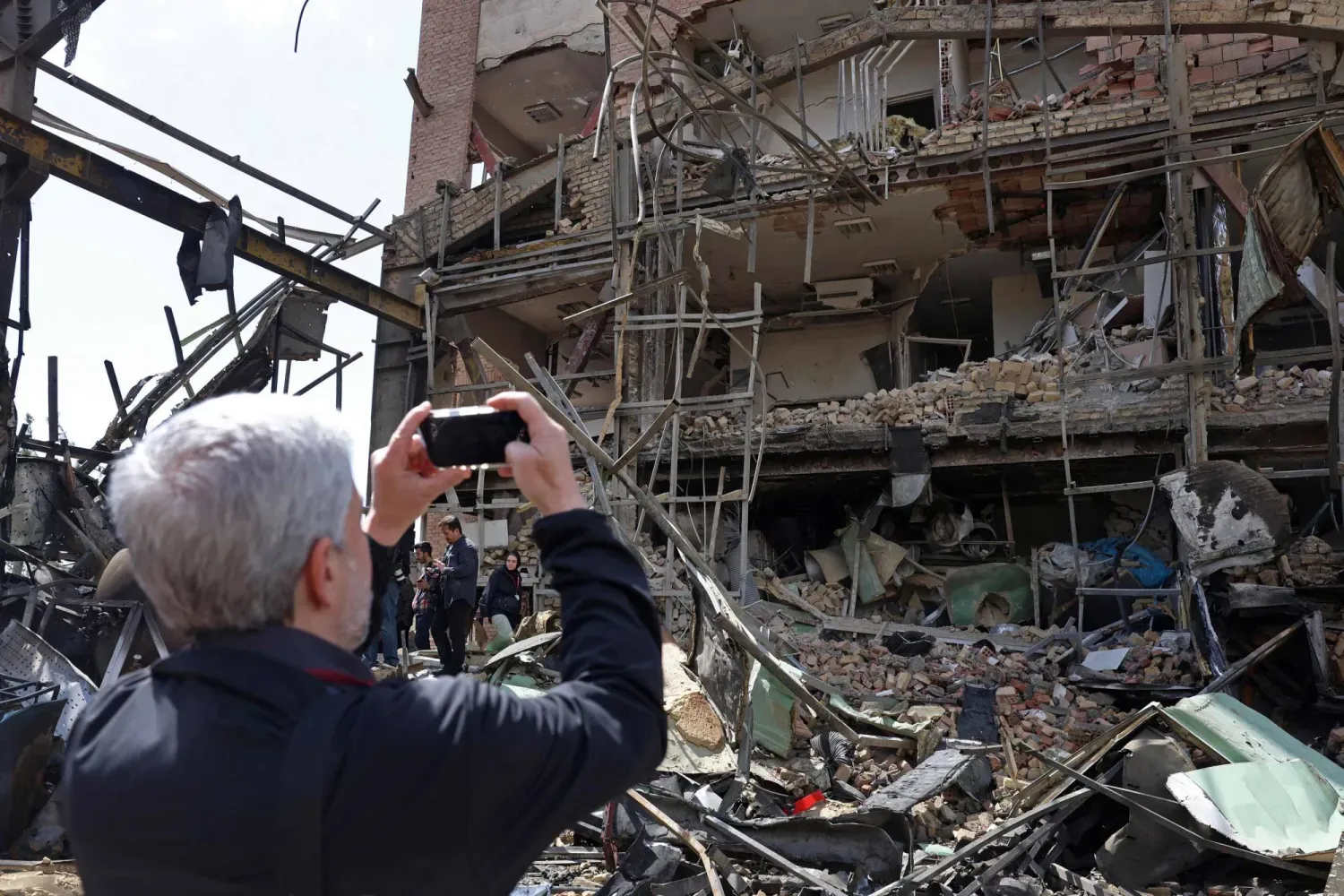 Tahran'da düzenlenen hava saldırısının ardından hasar gören Şehit Beheşti Üniversitesi binasının fotoğraflarını çeken bir adam (AFP)