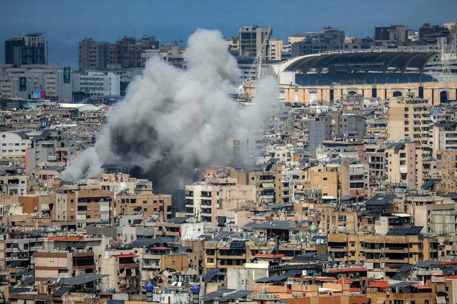 Smoke rises from the site of an Israeli strike in Beirut's southern suburbs, near Camille Chamoun Sports City stadium (R), on April 6, 2026. (AFP)