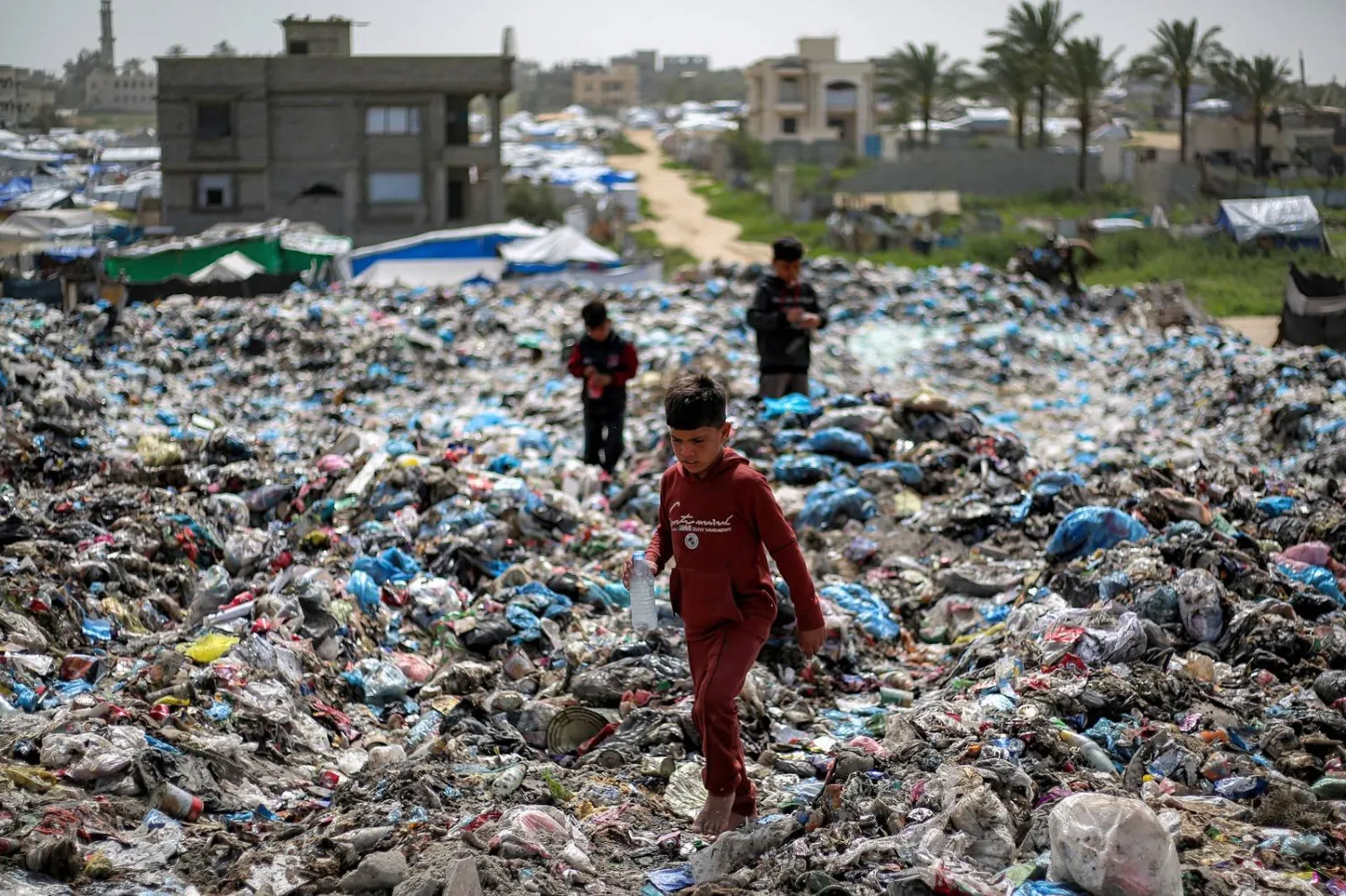 أطفال يبحثون عن مواد قابلة للتدوير في ساحة نفايات بمخيم البريج للاجئين الفلسطينيين بغزة (أ.ف.ب)