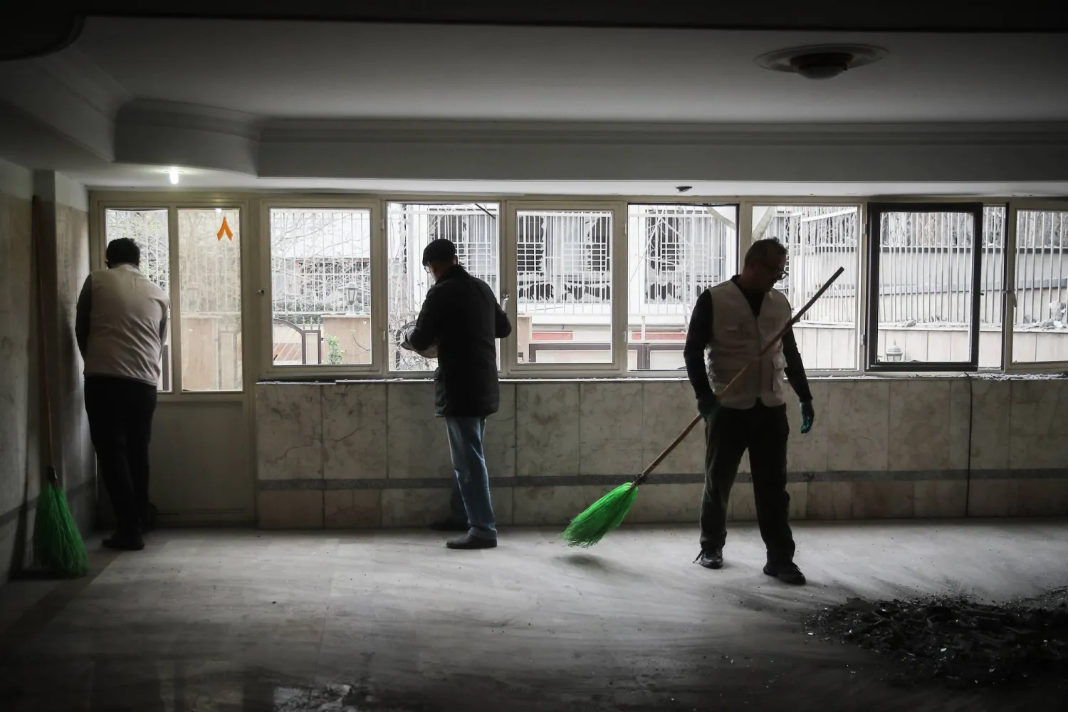 رجال إيرانيون ينظفون شقة داخل مبنى سكني تعرض لغارة جوية في طهران وسط الحرب الأميركية - الإسرائيلية على إيران (د.ب.أ)