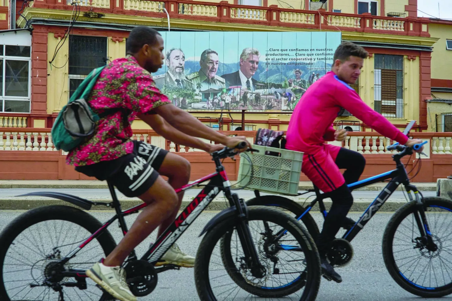 درّاجان يمرّان بجدارية للزعيم الكوبي الراحل فيديل كاسترو وخلفه راؤول كاسترو والرئيس الحالي ميغيل دياز كانل وسط هافانا (أ.ب)