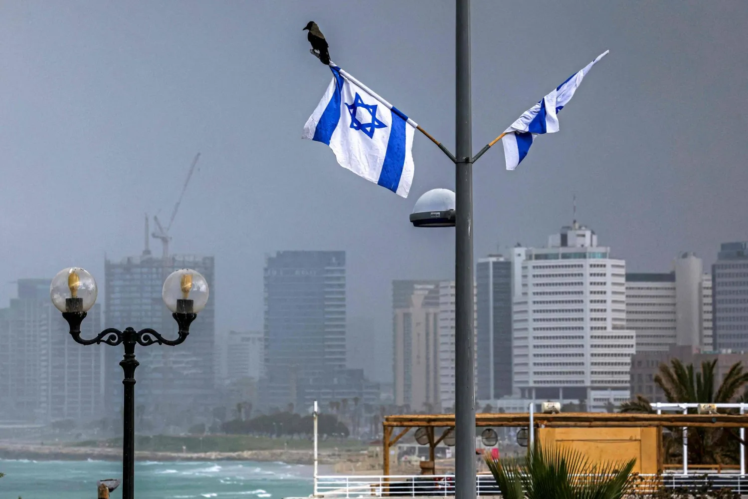A crow perches on an Israeli flag near an empty beach along the Tel Aviv coastline on April 7, 2026. (AFP)
