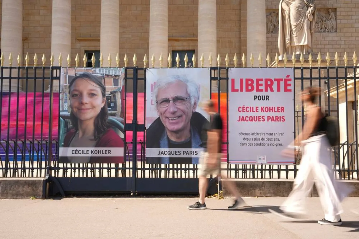 People walk past the portraits of French nationals Cecile Kohler and Jacques Paris in front of the French National Assembly in Paris on July 3, 2025. (AP)