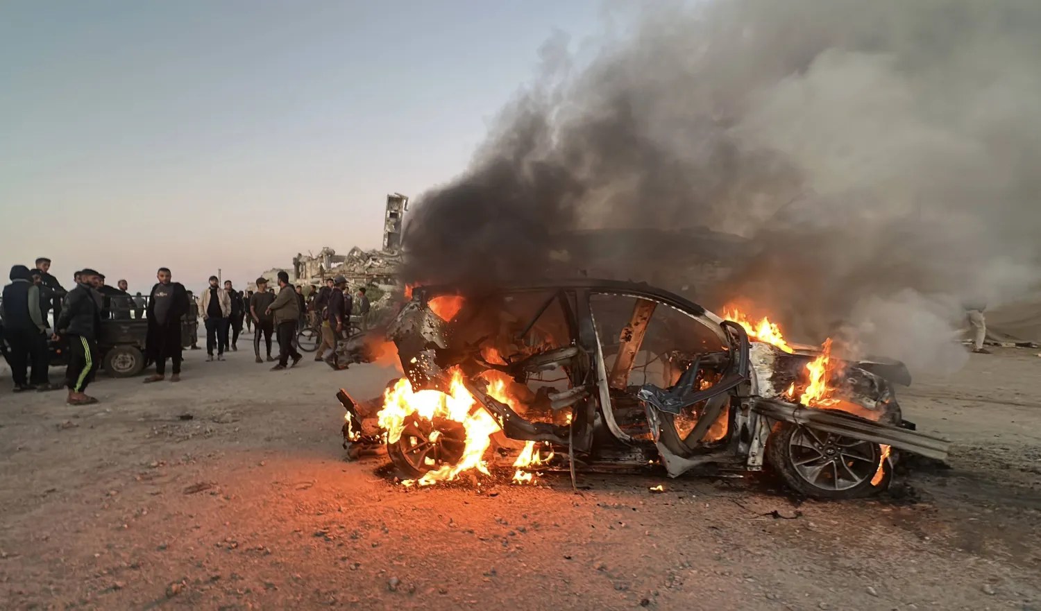يقف الناس قرب سيارة محترقة عقب غارة إسرائيلية أسفرت عن مقتل في قناة الجزيرة (د.ب.أ)