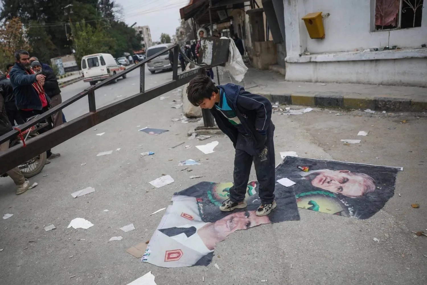 FILE -A boy steps over pictures of Syrian President Bashar Assad and his late father, Hafez Assad, right, Salamiyah, east of Hama, Syria, Dec. 7, 2024. (AP Photo/Ghaith Alsayed, File) 
