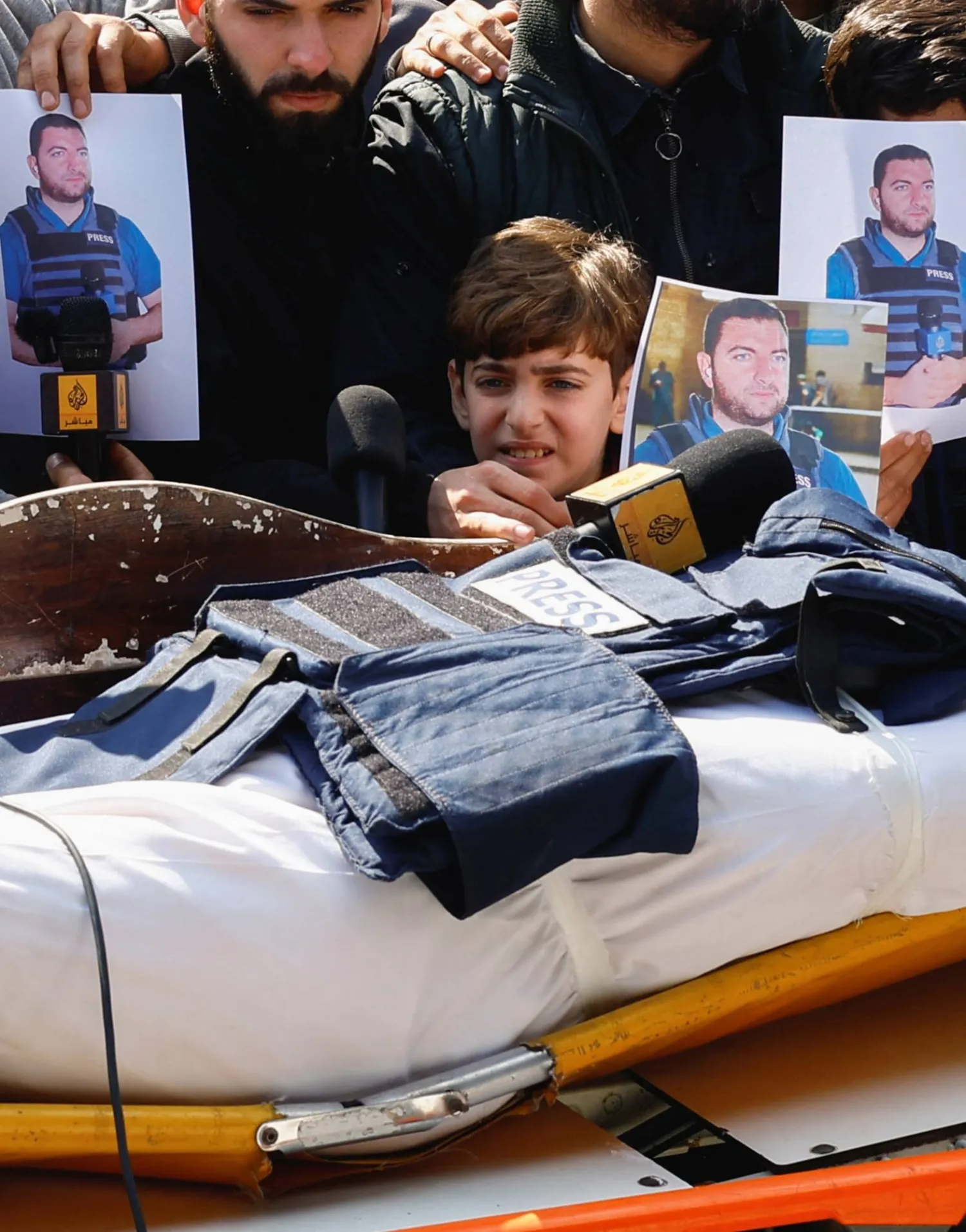 ينظر ابن الصحافي محمد وشاح نحو سترة وميكروفون موضوعين على جثمان والده خلال جنازته في مستشفى شهداء الأقصى بدير البلح (رويترز)