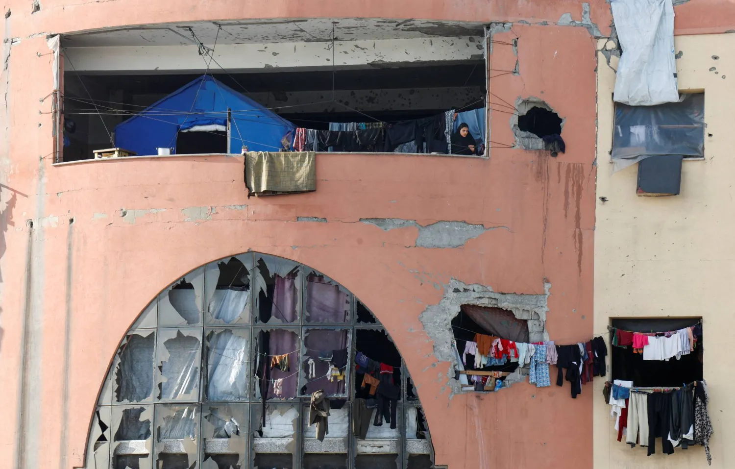 امرأة فلسطينية نازحة تقف على شرفة داخل مبنى مهدم في جامعة الأقصى جنوب غزة يُستخدم كمأوى (رويترز)