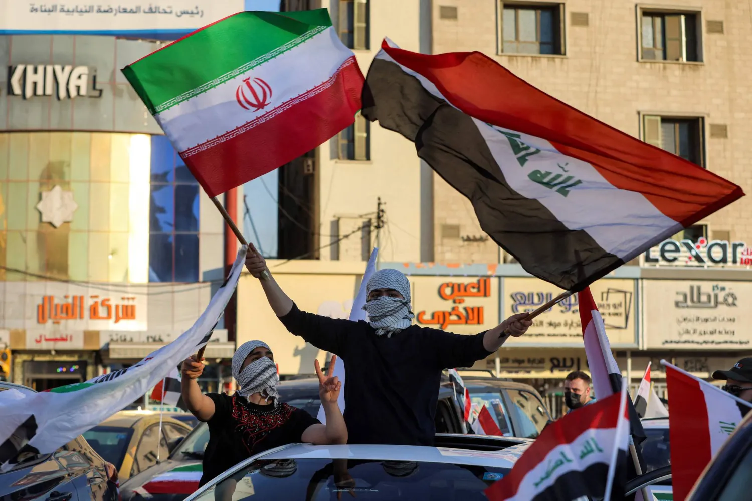 A man waves the flags of Iraq and Iran from the sunroof of a vehicle during celebrations welcoming the two-week ceasefire between the United States and Iran in Baghdad's central Tahrir Square on April 8, 2026. (AFP)