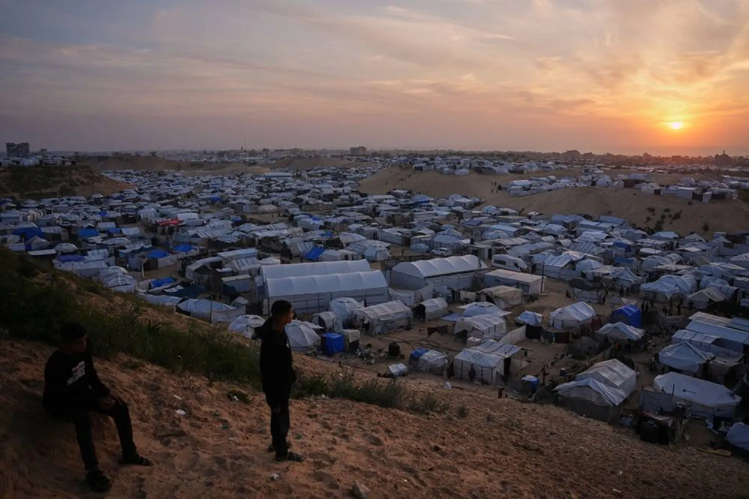  Palestinian youths look on as they stand in an area next to tents at a makeshift camp for displaced people, at sunset in Khan Younis, southern Gaza Strip, Thursday, April 9, 2026. (AP) 