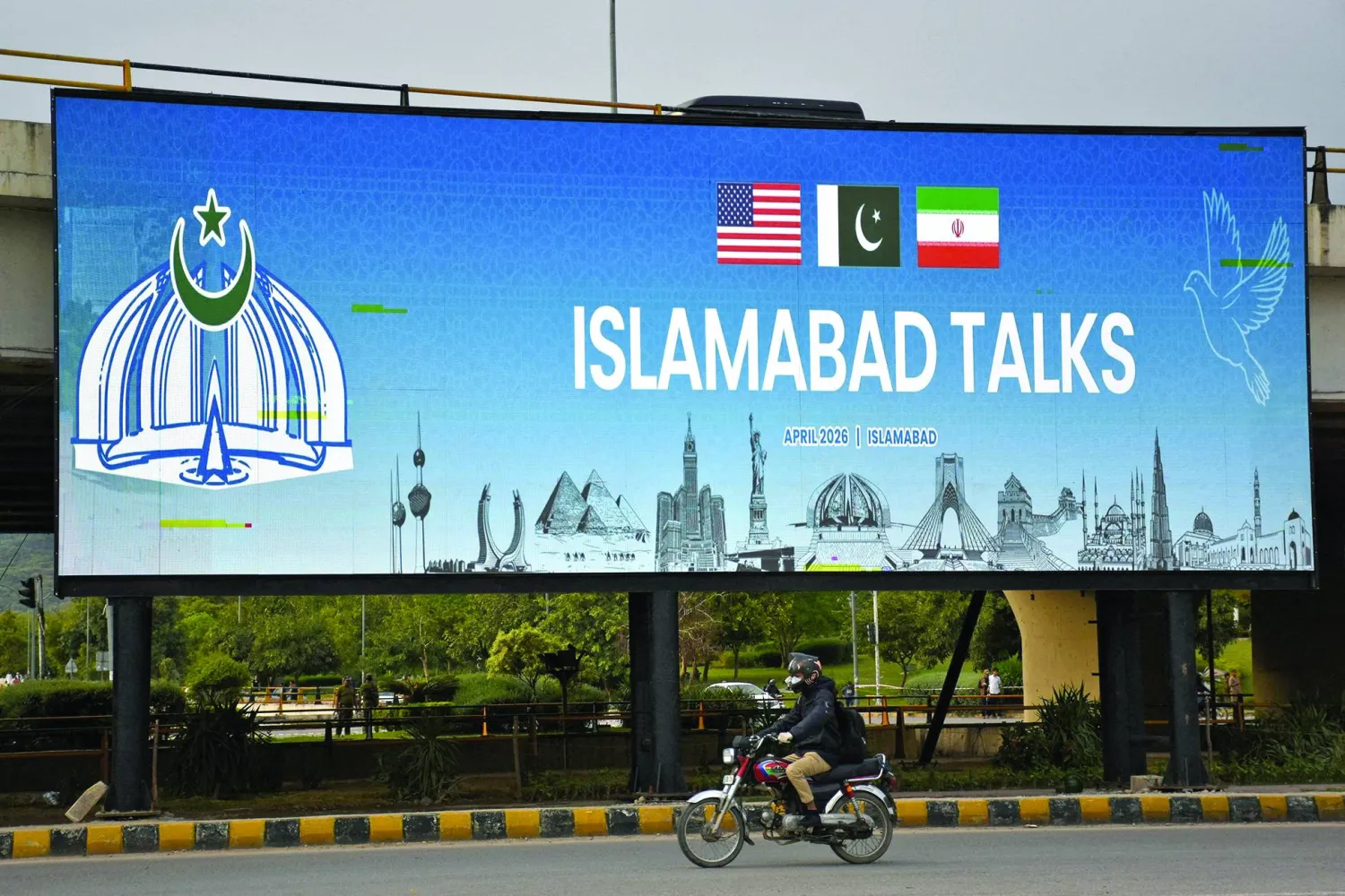 A man rides his motorbike past a billboard installed alongside a road as Pakistan prepares to host the US and Iran for peace talks, in Islamabad, Pakistan, April 10, 2026. REUTERS/Waseem Khan 