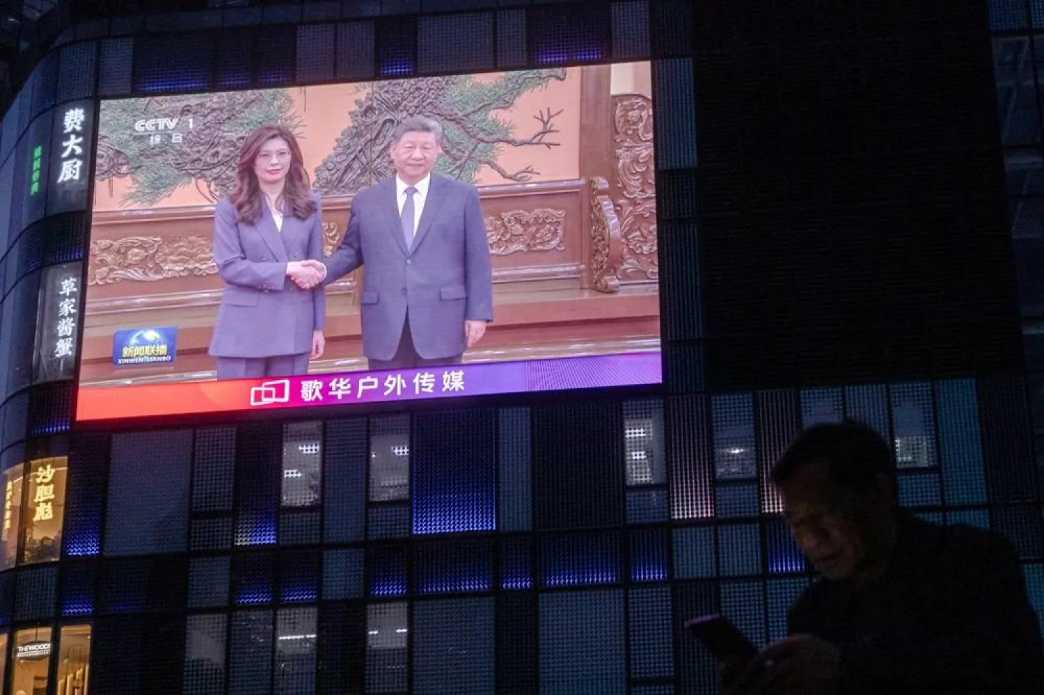  A man uses his smartphone as a giant screen broadcasts news showing Chinese President Xi Jinping shaking hands with Cheng Li-wun, chairperson of the Kuomintang (KMT), Taiwan's largest opposition party at the Great Hall of the People in Beijing, China, April 10, 2026. (Reuters)