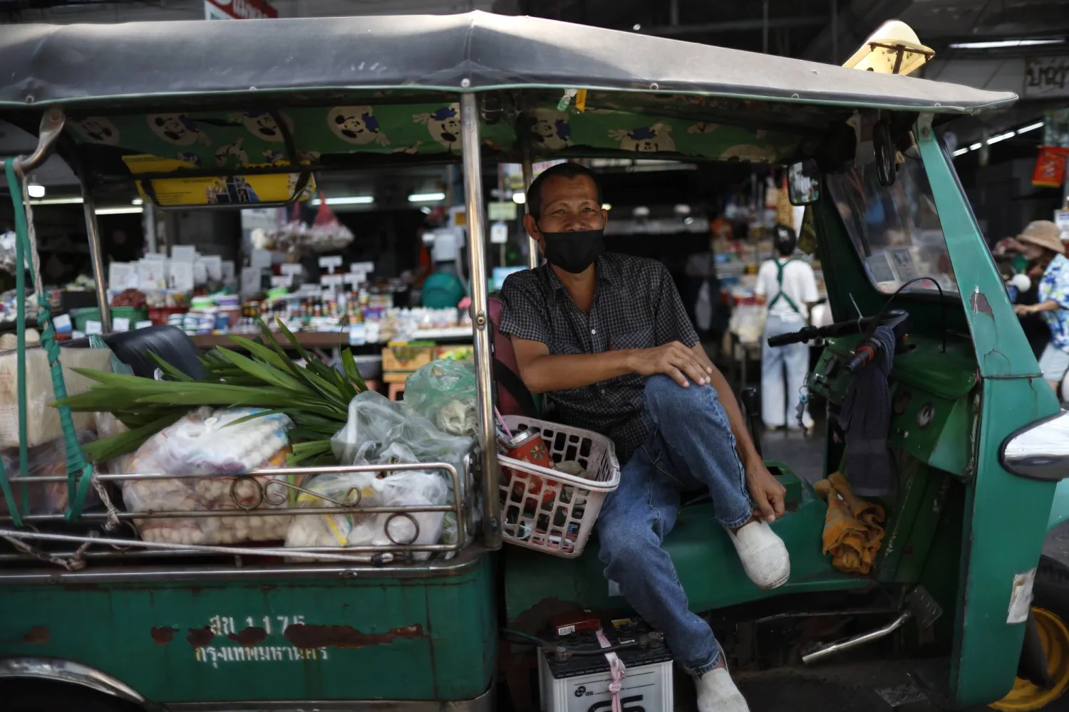 سائق توك توك وهي مركبة أجرة ثلاثية العجلات ينتظر ركاباً يشترون الطعام في سوق ببانكوك (إ.ب.أ)