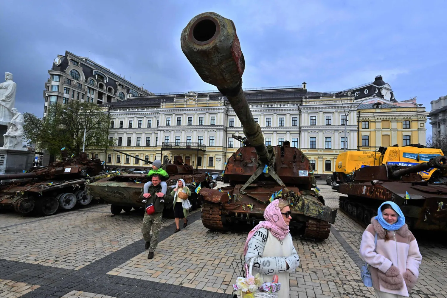 سكان يحملون سلالهم المليئة بالكعك والبيض التقليديين في أثناء مرورهم بمعرض للمعدات العسكرية الروسية المدمرة خلال احتفالات عيد الفصح في كييف الأحد (أ.ف.ب)