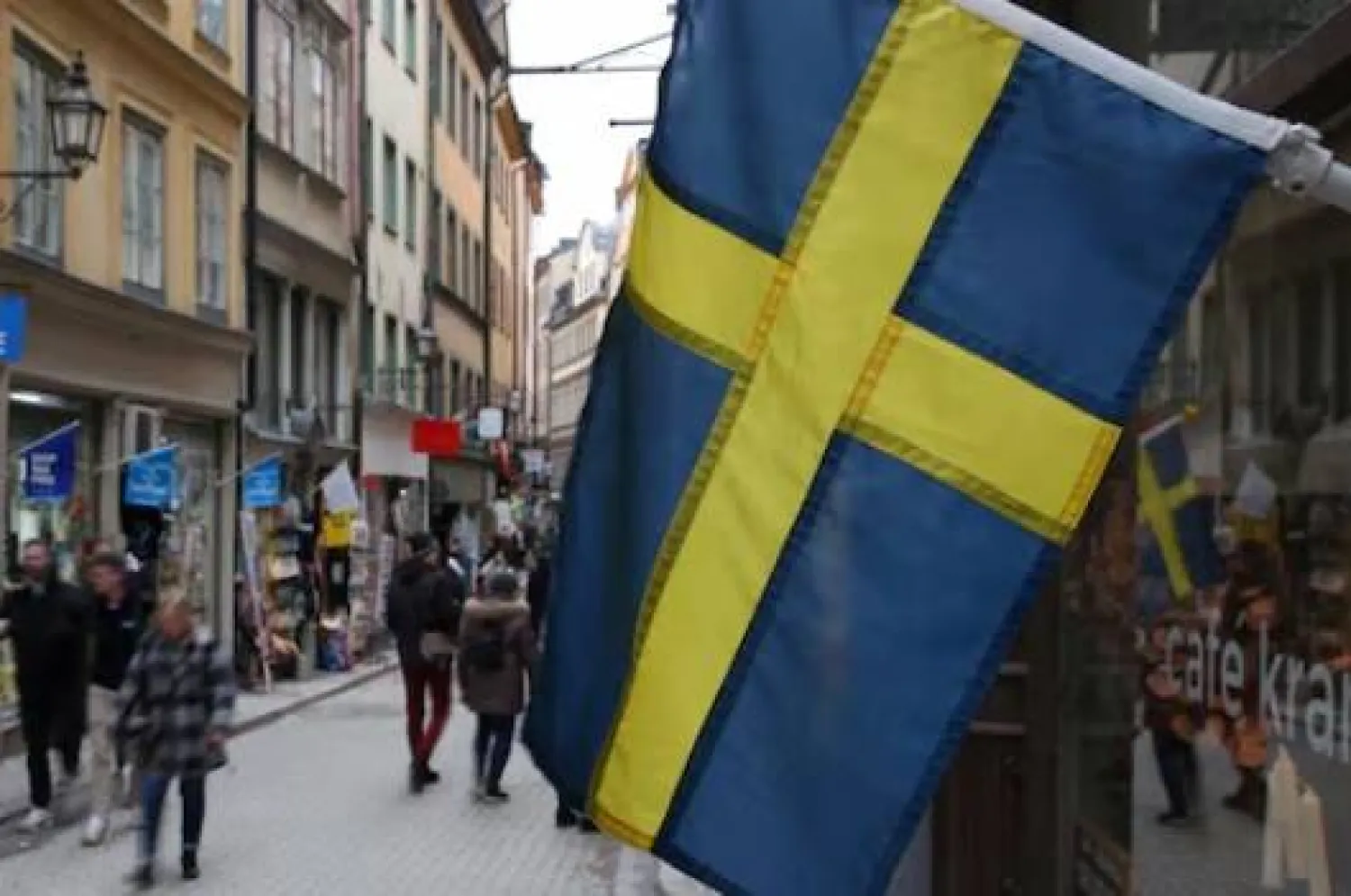 علم سويدي مُعلَّق خارج متجر بأحد شوارع المدينة القديمة في ستوكهولم (رويترز)