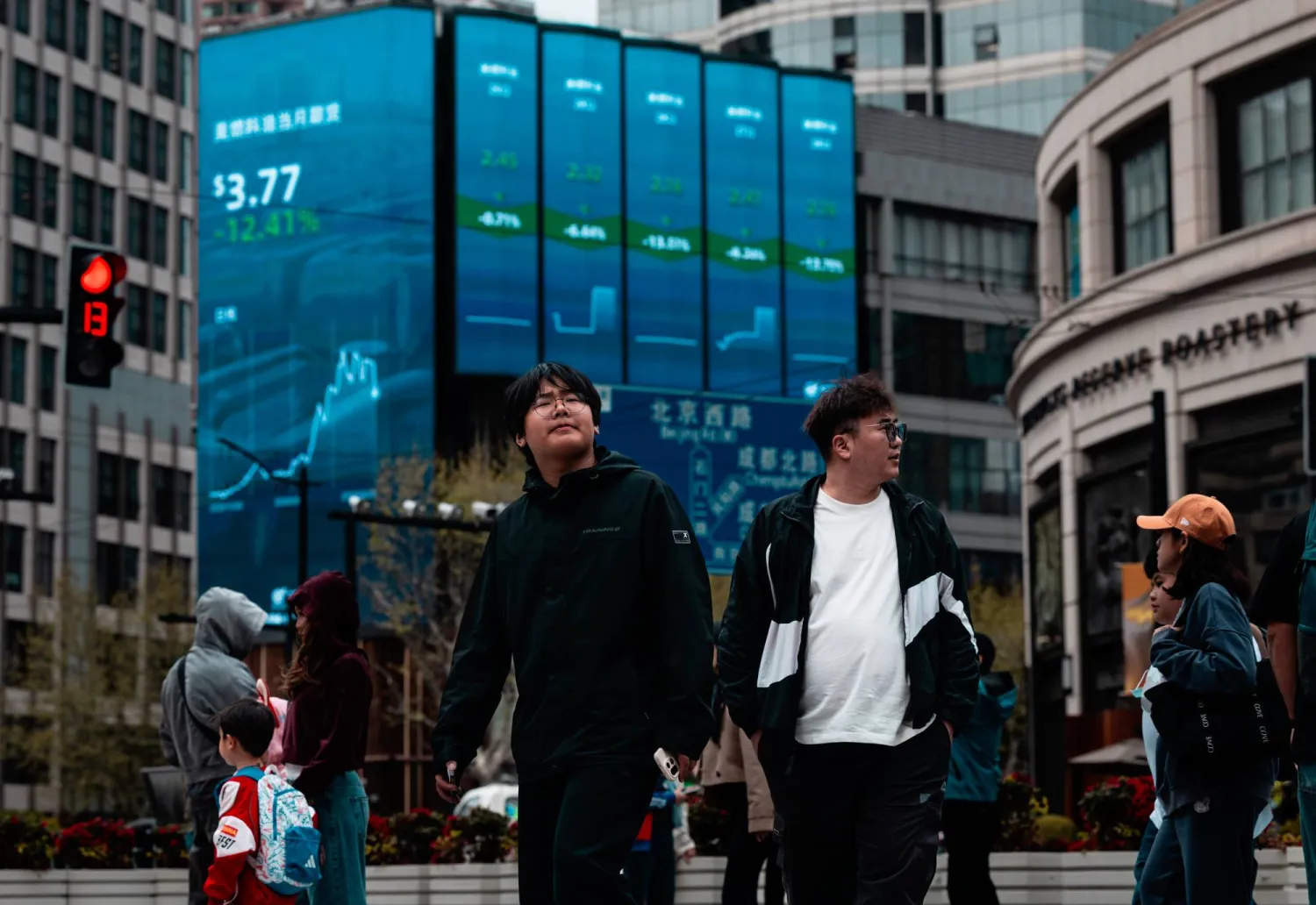 مشاة يعبرون الطريق أمام شاشة تعرض حركة الأسهم في مدينة شنغهاي الصينية (إ.ب.أ)