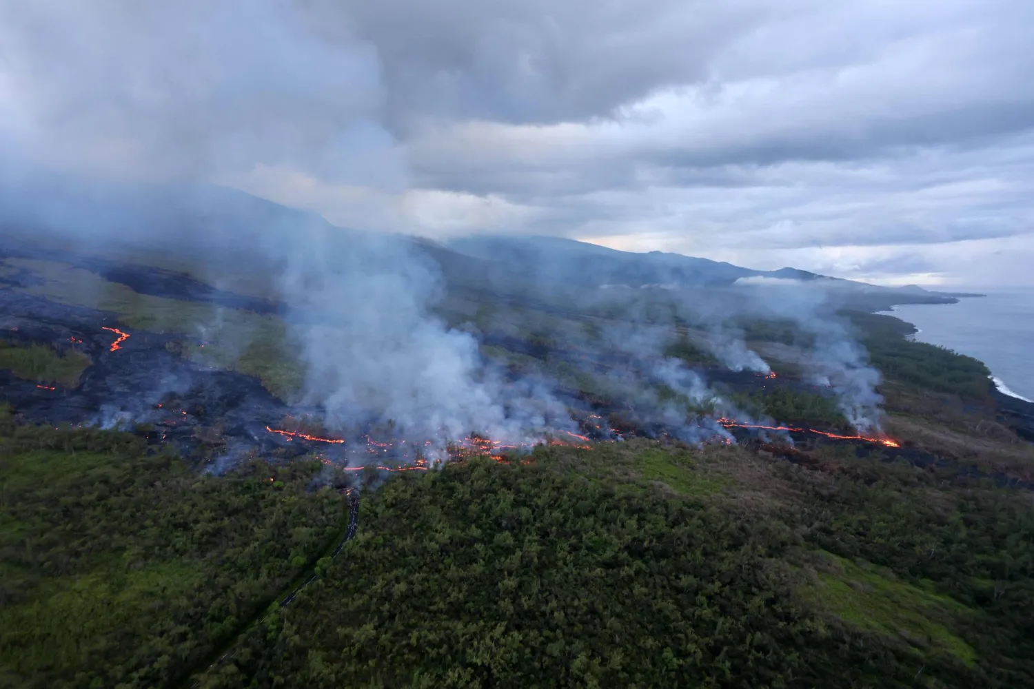 An aerial picture shows smoke rising as lava from the Piton de la Fournaise volcano  comes to a halt in Saint-Philippe, on the French Indian ocean island of Reunion, on April 2, 2026. (Photo by Richard BOUHET / AFP)