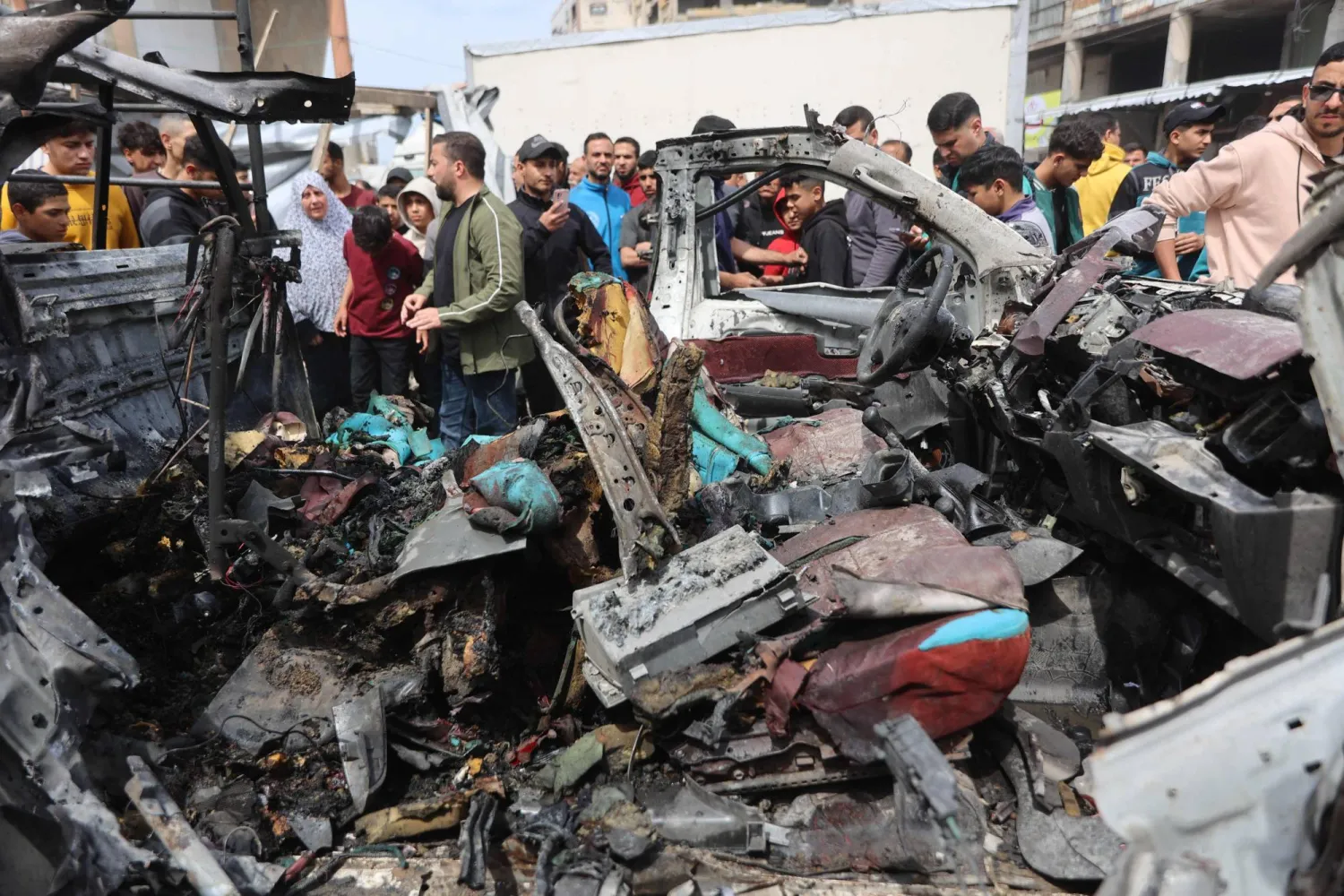 فلسطينيون يتجمعون حول حطام سيارة الشرطة التي دُمرت في الغارة الإسرائيلية (أ.ف.ب)