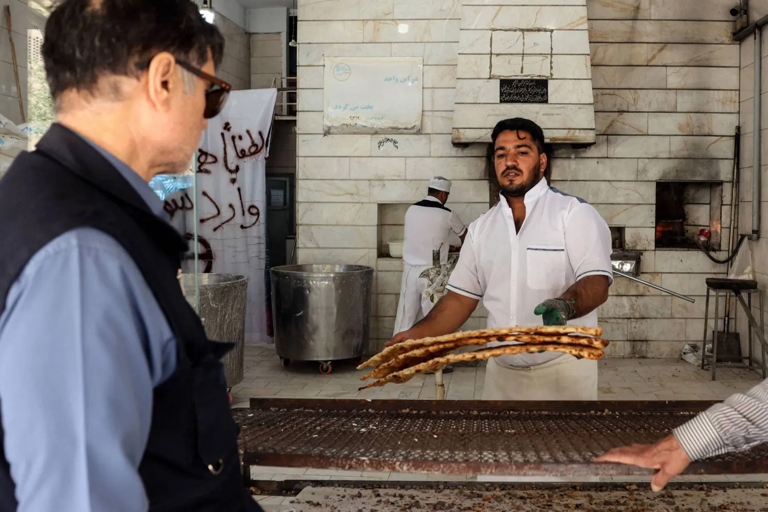 عامل يقدم الخبز للزبائن في مخبز جنوب طهران (أ.ف.ب)