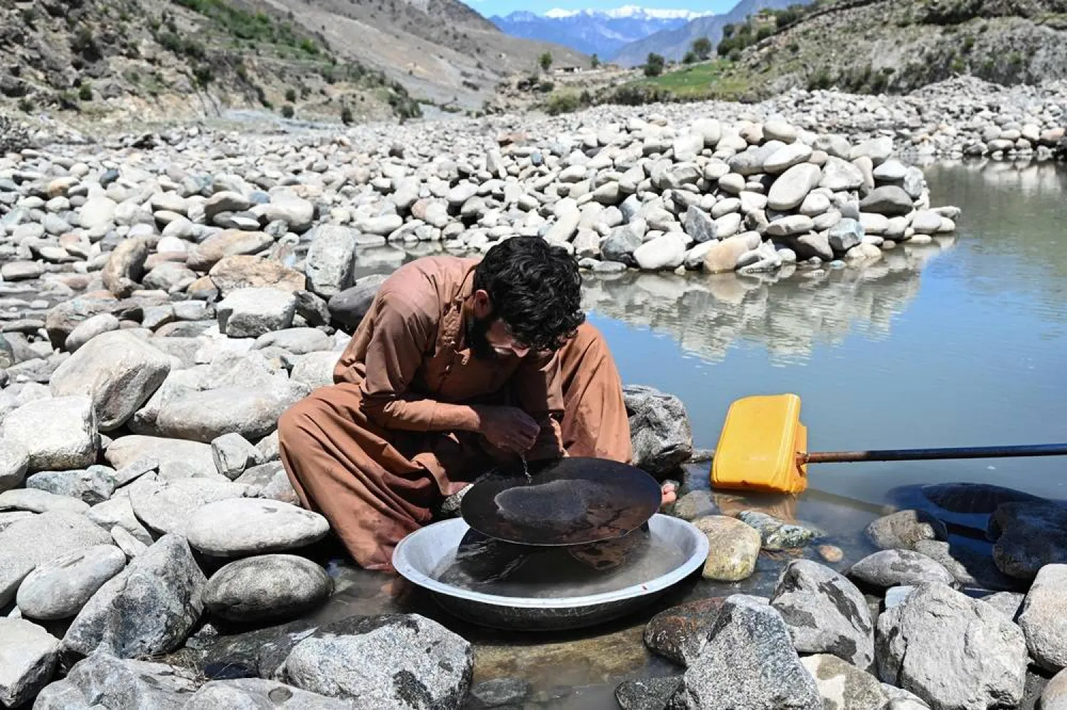 This photograph taken on April 13, 2026 shows an Afghan man scouring for gold using the traditional gold-panning technique, after sorting nuggets from mountainside stones excavated from the Kunar riverbed in the Kharwalu area of Naray district, Kunar province. (AFP)