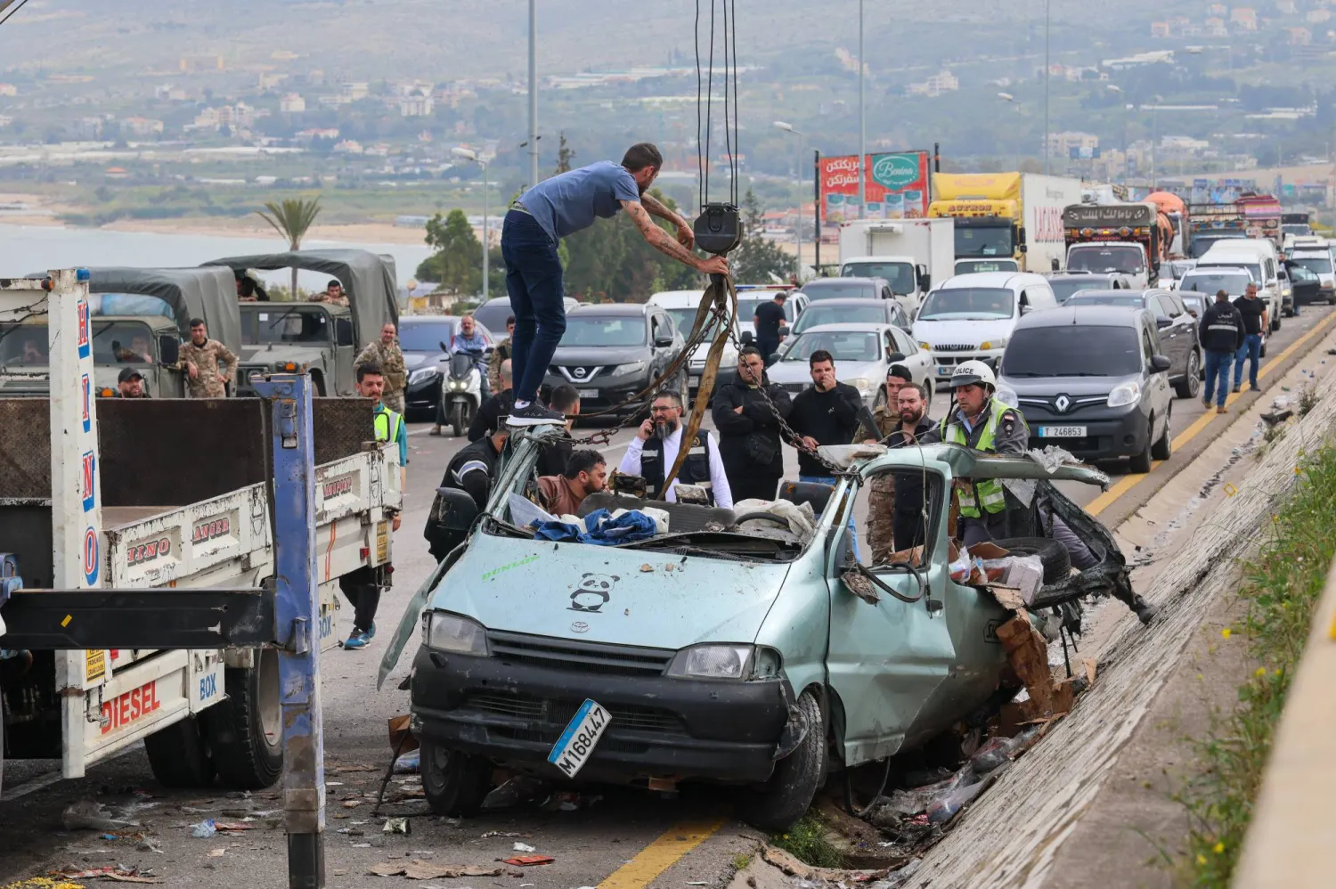 أشخاص يزيلون حطام سيارة من موقع استهدافها بغارة إسرائيلية في بلدة السعديات جنوب بيروت (إ.ب.أ)