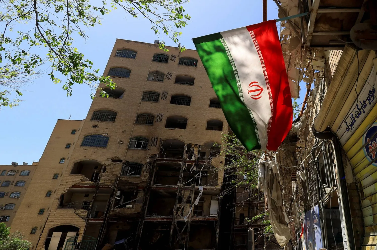 علم إيراني يظهر بالقرب من مبنى سكني تضرر جراء غارة جوية على طهران (رويترز)