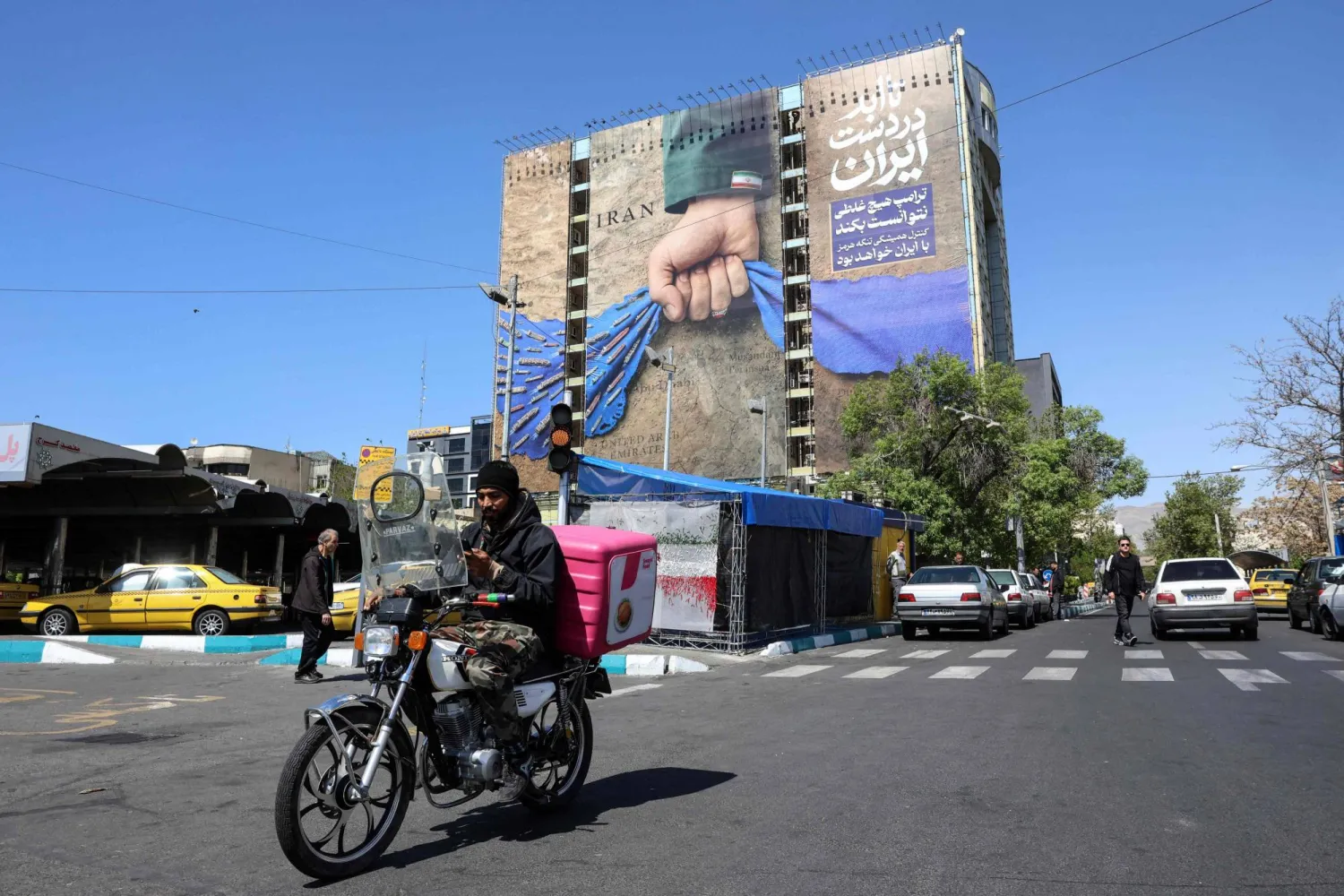 A man rides past a large billboard referring to the Strait of Hormuz in Tehran's Vanak Square on April 15, 2026. (AFP)