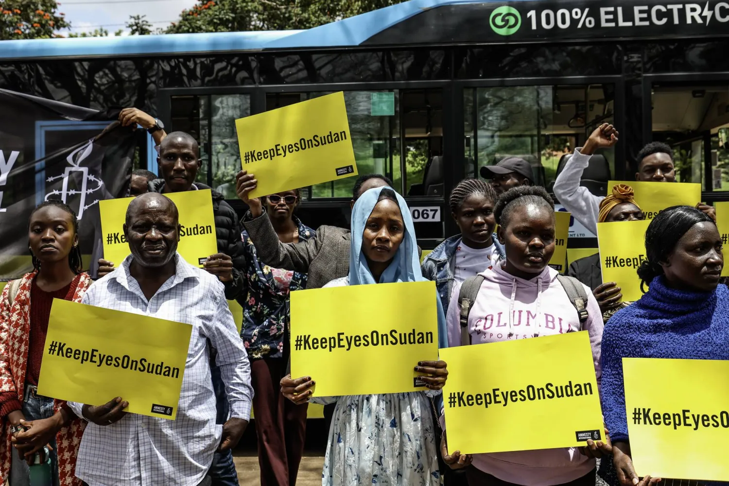 Some of the Sudanese civilian refugees and human rights activists hold placards with the wordings, 'KeepEyesOnSudan' outside a bus branded during a commemorative gathering dubbed 'Under the Neema (Tree)' to mark the third anniversary since the war in Sudan started, organized by the Amnesty International at the Freedom Corner in Nairobi, Kenya, 15 April 2026. EPA/DANIEL IRUNGU