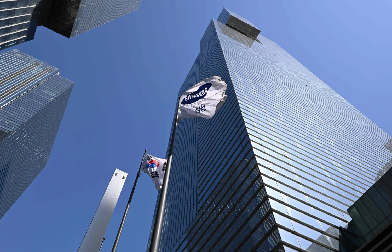 A South Korean national flag (L) and a Samsung flag (R) flutter outside the company's Seocho building in Seoul on April 7, 2026. (Photo by Jung Yeon-je / AFP)