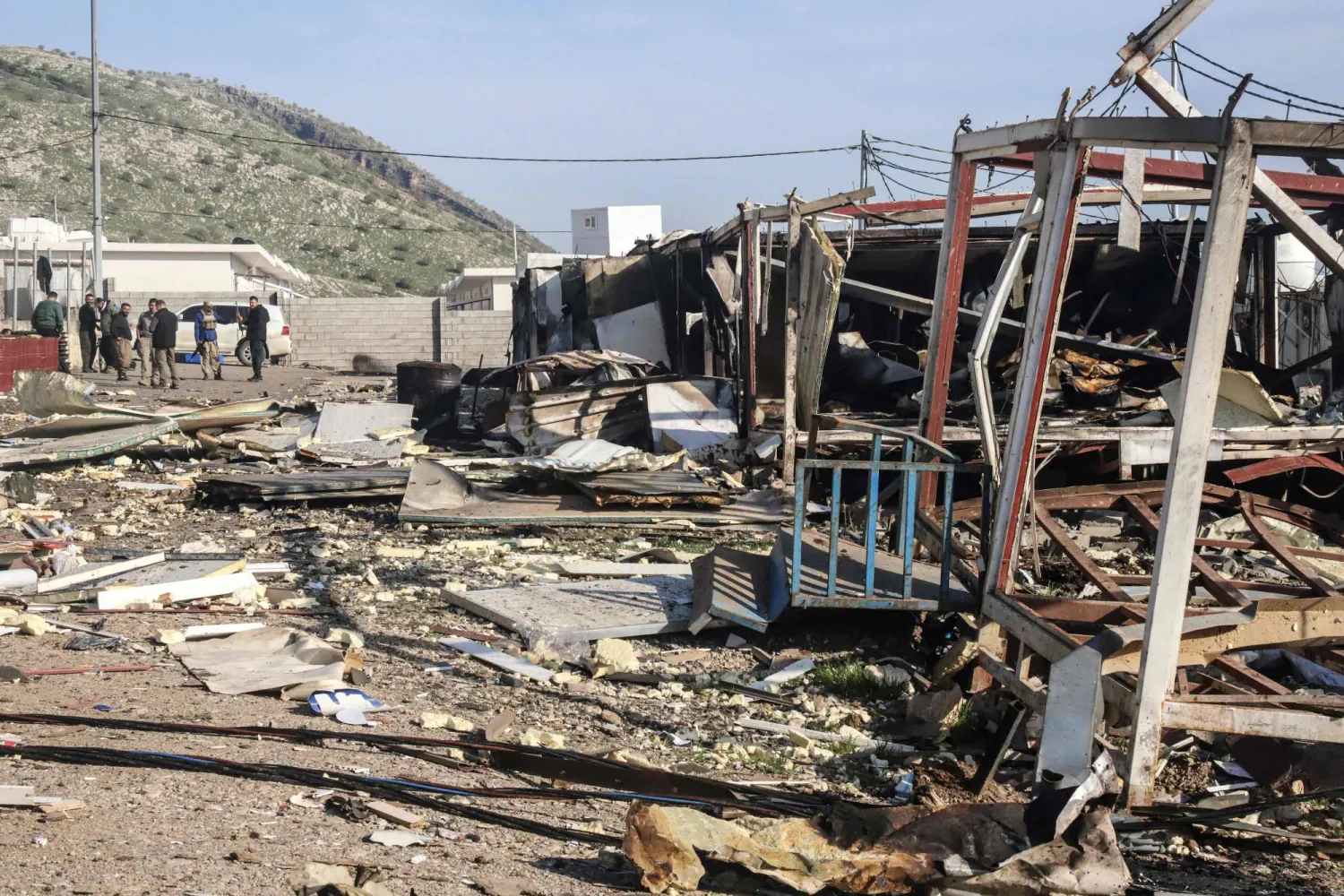 Komala party members look towards the debris is strewn from mangled structures following drone strikes on the Iranian Kurdish opposition Komala party's Sordash camp, which resulted in the death of a female party member and the injury of two others, some 40 km northwest of the city of Sulaymaniyah in the autonomous Kurdistan region on April 15, 2026. (AFP)