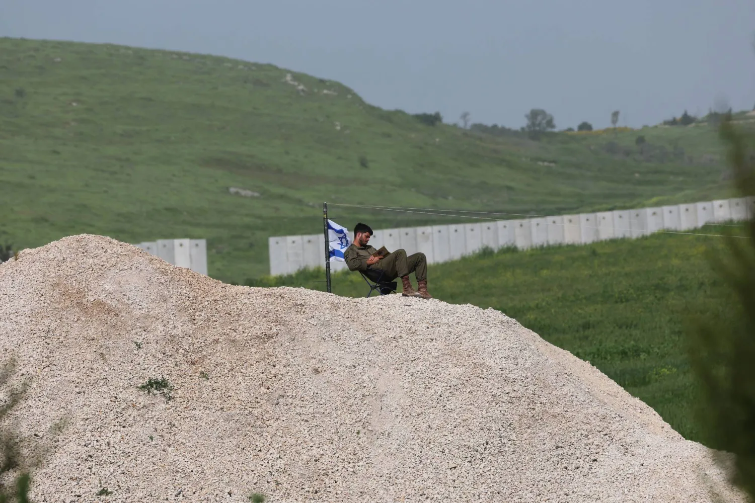 جندي إسرائيلي بجوار العلم الإسرائيلي قرب الحاجز الأمني ​​بين إسرائيل ولبنان بالقرب من أفيفيم شمال إسرائيل (إ.ب.أ)