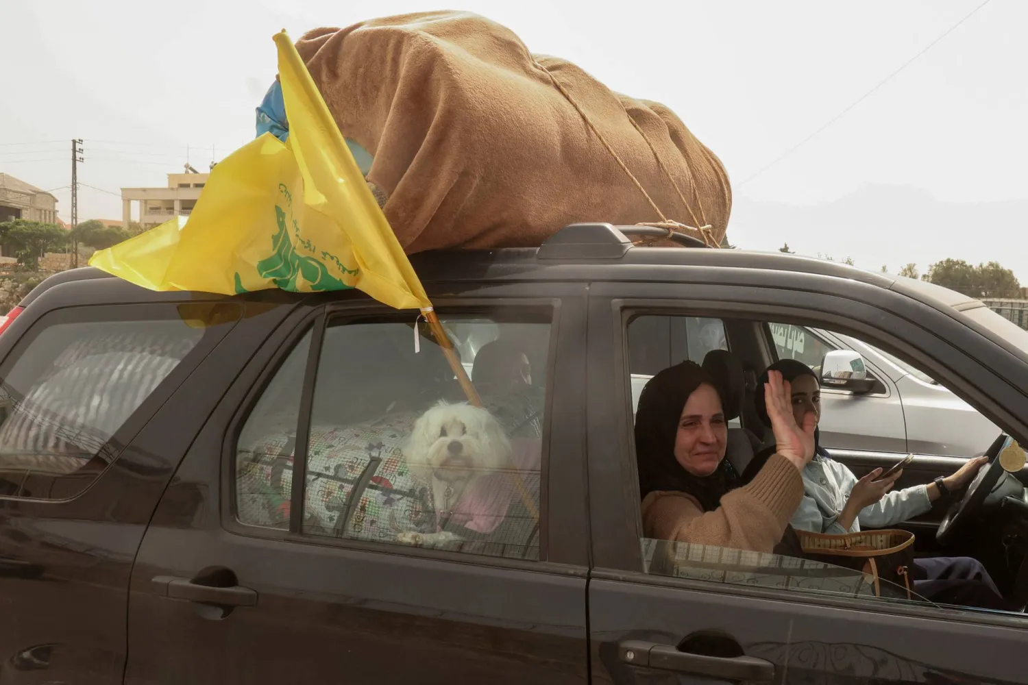 عائلة نازحة خلال عودتها إلى قريتها في الجنوب إثر الإعلان عن الهدنة وهي ترفع علم «حزب الله» على السيارة (رويترز)